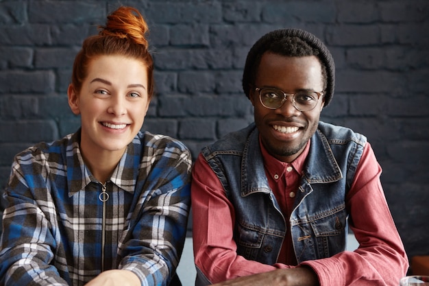 Free photo two friends relaxing at cafe, sitting at table close to each other against black brick wall