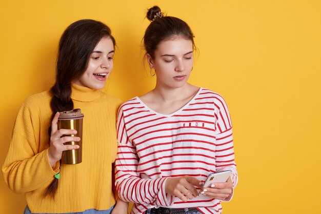 Two friends sharing smart phone and drinking coffee together, posing