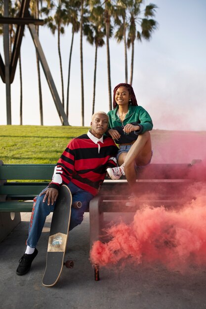 Two friends sitting on a bench with their skateboards and a smoke bomb outside in the park