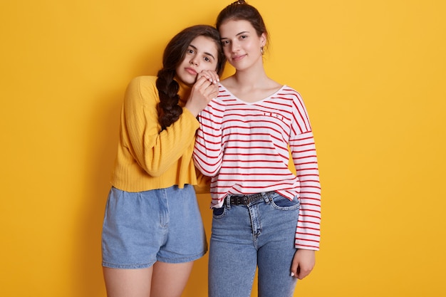 Free photo two friends wearing stylish clothing standing isolated over yellow wall