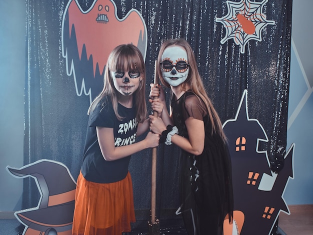 Two friends with festive halloween makeup are posing for photographer on the decorations background.