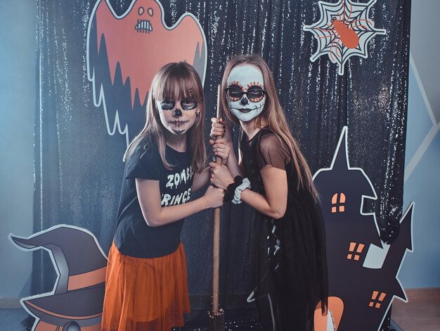 Two friends with festive Halloween makeup are posing for photographer on the decorations background.