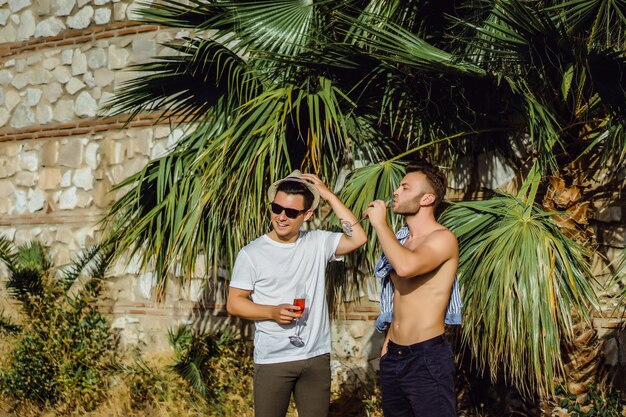 two friends, young men with glasses of champagne on the background of tropical greenery