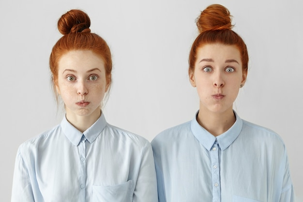 Two funny bug-eyed young European females with same hairstyles, dressed in identical shirts