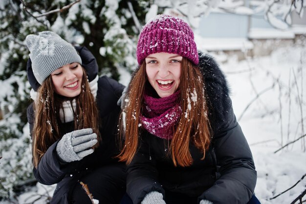 雪に覆われた木の近くで冬の雪の日に楽しんでいる2人の面白いガールフレンド