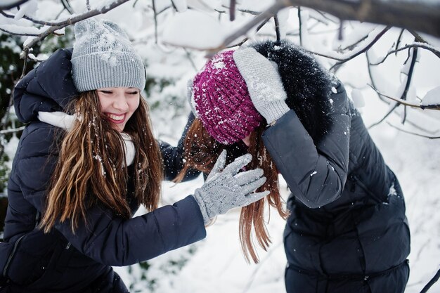 Two funny girls friends having fun at winter snowy day near snow covered trees