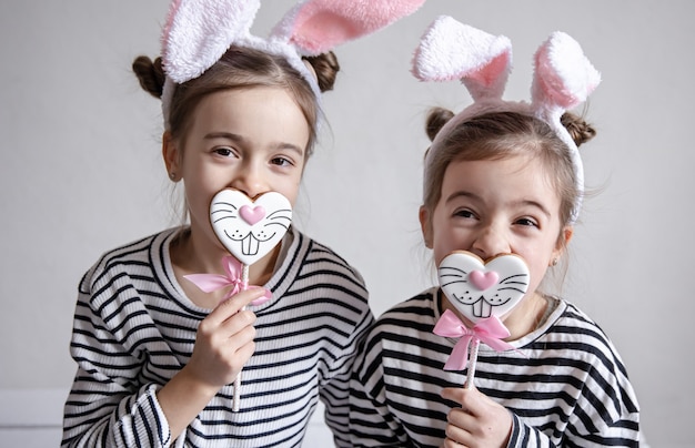 Two funny little sisters are posing with Easter gingerbread in the form of bunny faces.