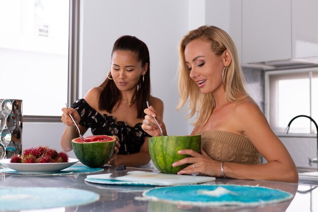 キッチンでスイカとランブータンのトロピカルフルーツを食べる2人のガールフレンド