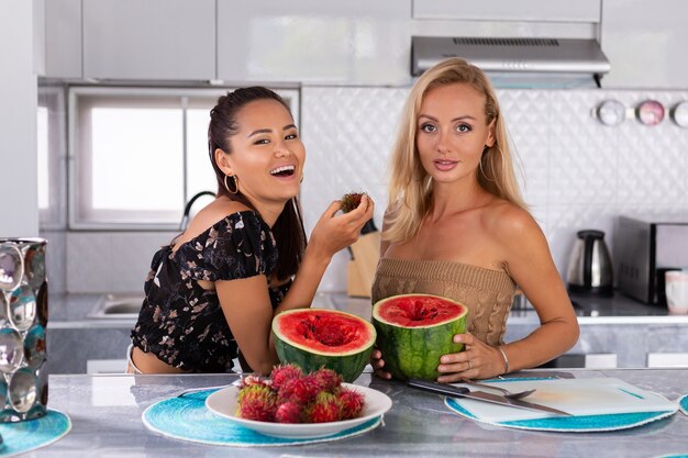 부엌에서 수박과 람부탄 열대 과일을 먹는 두 여자 친구
