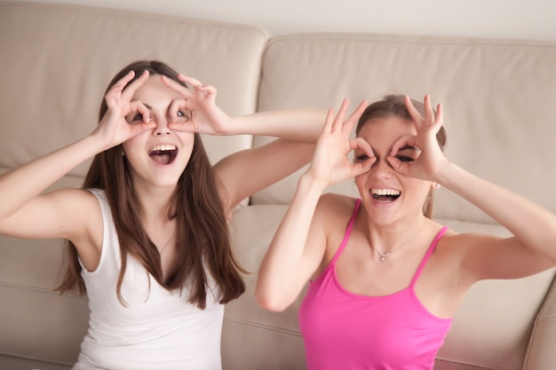Две подружки глупо делают очки с пальцами.