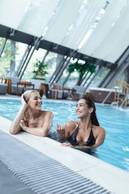 실내 수영장에서 여름 휴가를 즐기는 수영장 옆에 앉아 수영복을 입은 두 여자