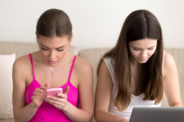 Two girlfriends using mobile phone and laptop