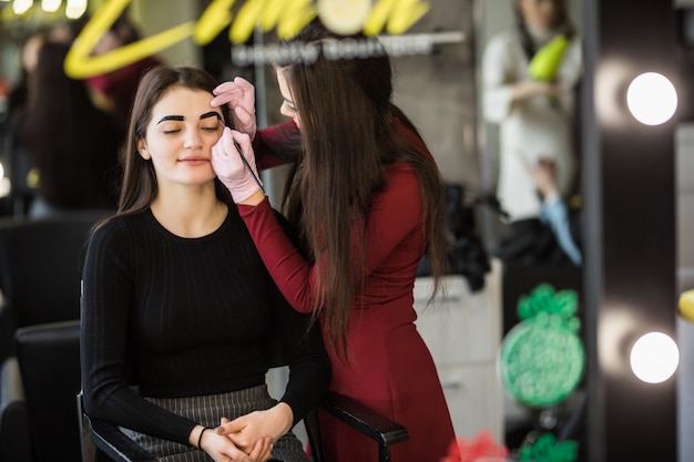 Two girls are doing make-up in front of big professional mirror