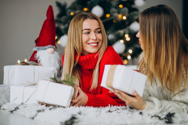 Two girls friends with christmas presents by the christmas tree