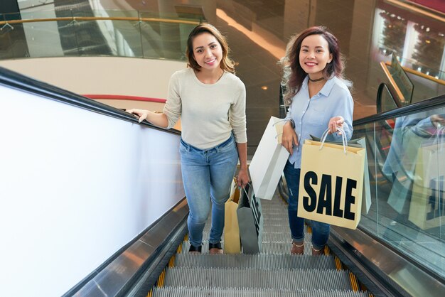 Две девушки поднимаются по лестнице на эскалаторе в торговом центре