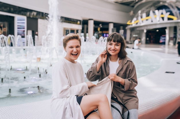 Две девушки развлекаются в торговом центре, у фонтана