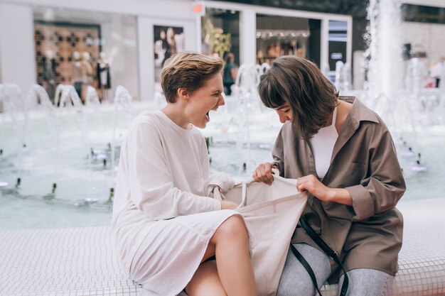 Two girls have fun in the mall, next to a fountain