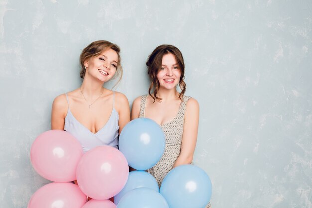 Due ragazze che si divertono in uno studio e giocano con palloncini blu e rosa.