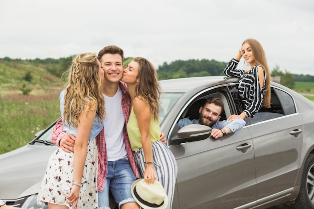 Two girls kissing her boyfriend standing near the car