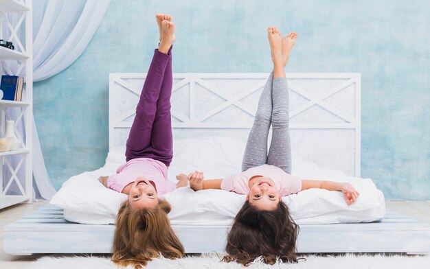 Two girls lying on bed with their crossed legs up at home