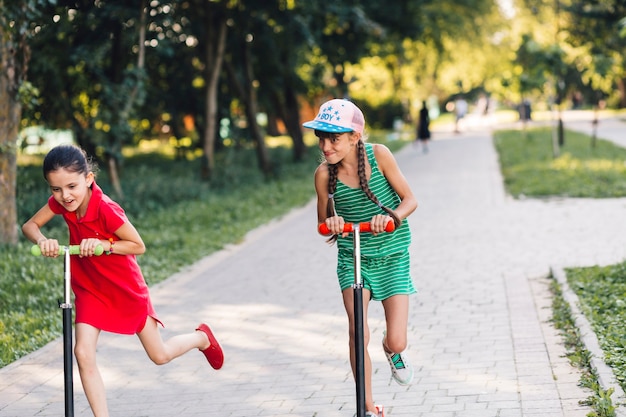 Two girls making fun while riding on kick scooter in the park