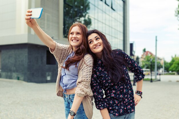 Two girls making funny selfie on the street, having fun together