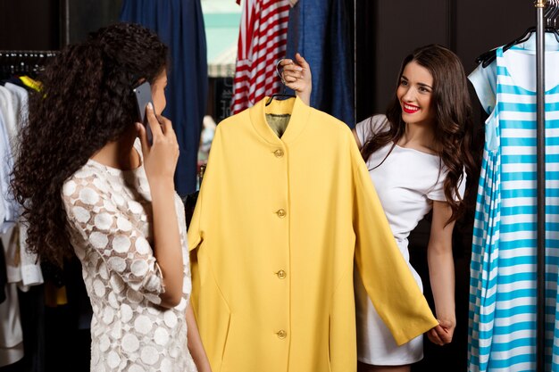 Two girls making shopping in mall. One speaking on phone.