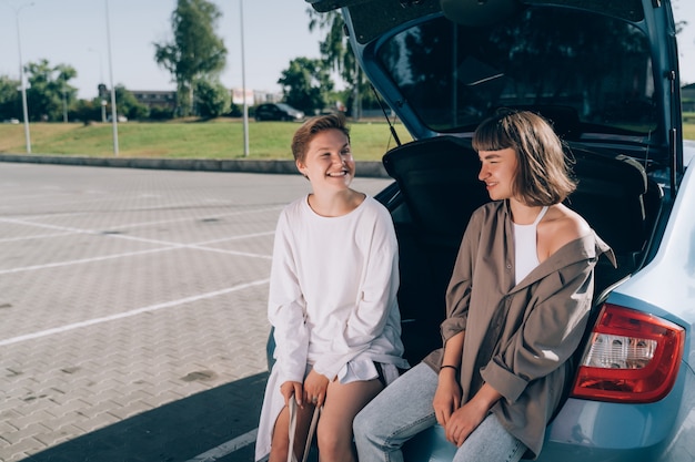 Two girls in the parking lot at the open trunk posing for the camera.