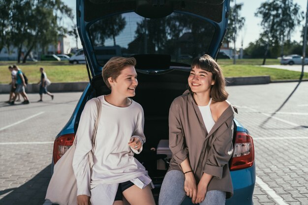 Two girls in the parking lot at the open trunk posing