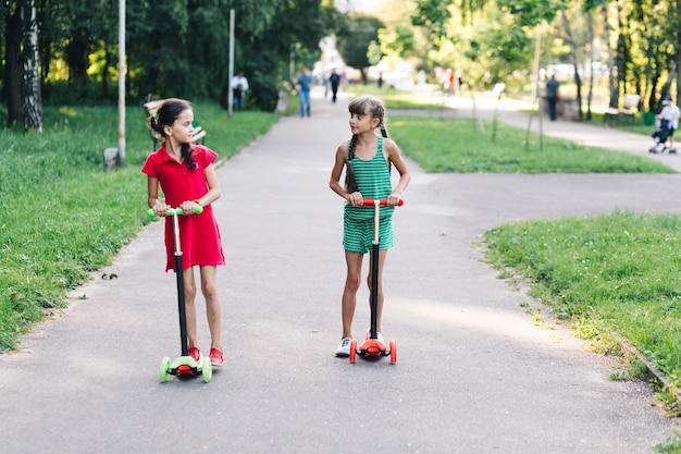 Two girls riding kick scooter in the park