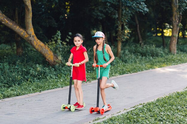 Two girls riding on push scooter in the park