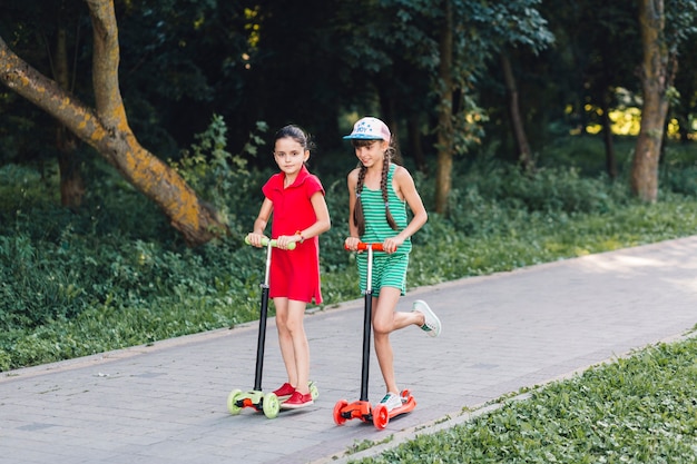 Two girls riding on push scooter in the park