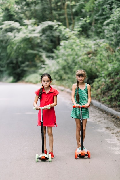 Two girls riding scooters on road