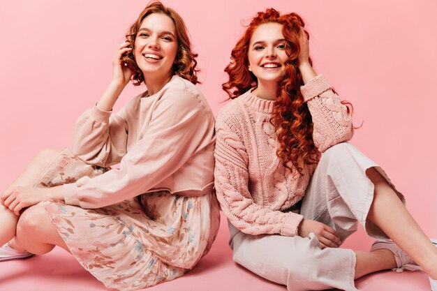 미소로 바닥에 앉아 두 여자입니다. 분홍색 배경에 포즈 친구의 스튜디오 샷입니다.