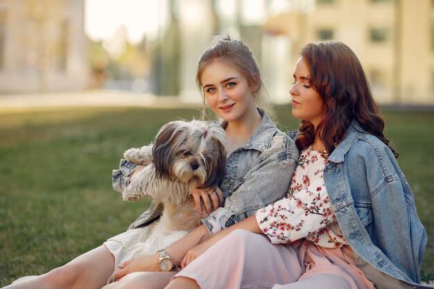Две девушки сидят в парке с маленькой собачкой
