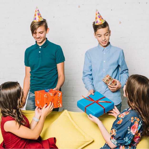 Two girls sitting on sofa giving presents to the smiling birthday boys