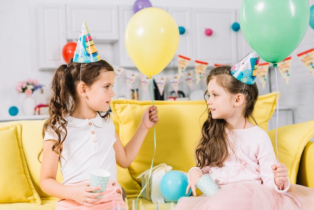 Two girls sitting on sofa holding balloon