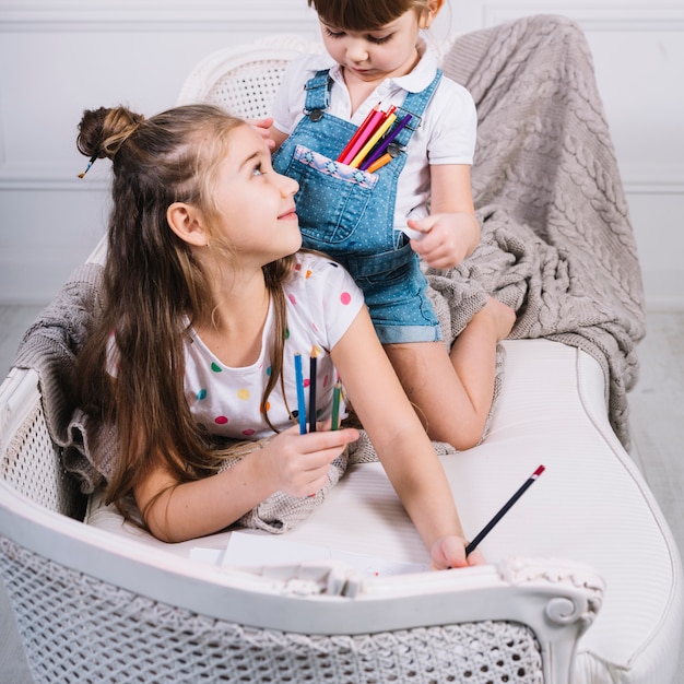 Free photo two girls sitting on sofa with pencils and paper