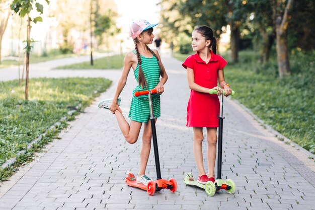 Two girls standing on push scooter in the park