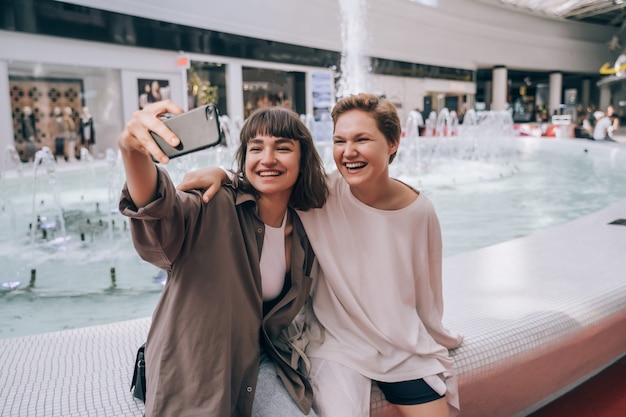 Две девушки делают селфи в торговом центре, у фонтана