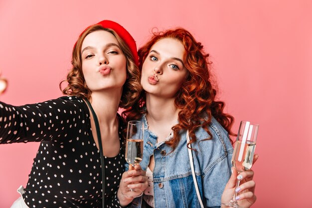 와인 잔으로 셀카를 복용하는 두 여자. 분홍색 배경에 샴페인을 마시는 친구의 스튜디오 샷.