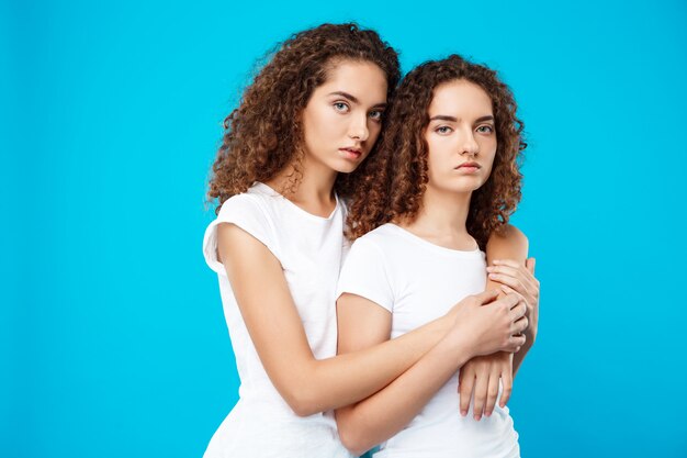 Two girls twins embracing over blue wall