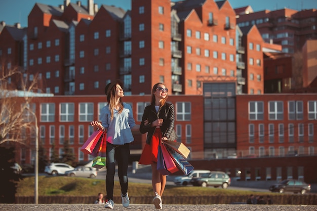 Two girls walking with shopping bags on city streets at sunny day