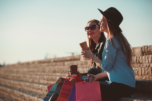 Two girls walking with shopping bags on city streets at sunny day