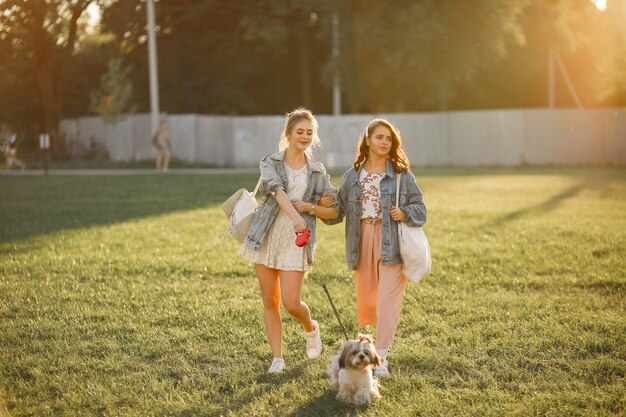 Two girls wallking in a park with a little dog