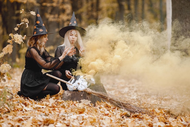 Two girls witches in forest on Halloween. Girls wearing black dresses and cone hats. Witches make a magic potion.