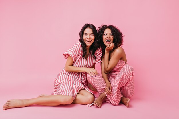 Two girls with dark hair, one with straight and other with curly, dressed in soft and lovely pajamas, having fun and playing