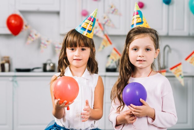 Two girls with red and purple balloons standing in kitchen