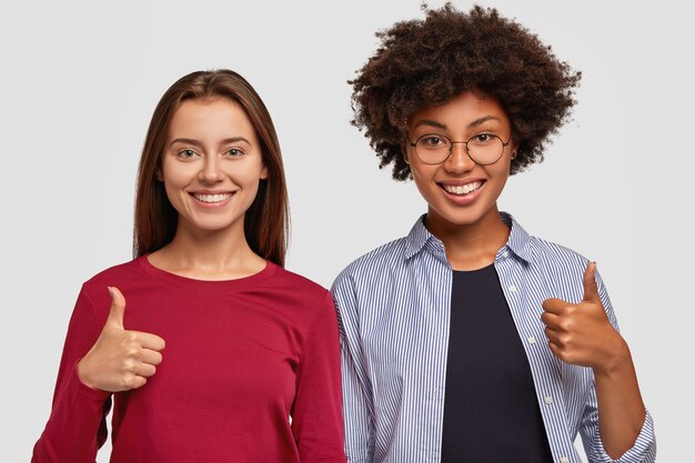 Two glad mixed race women show thumb up gesture with one hand