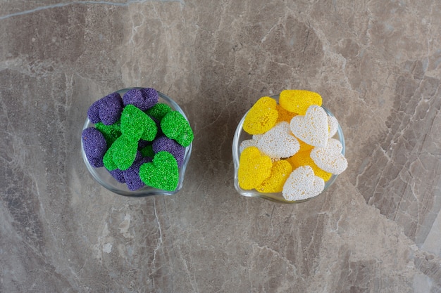 Two glass bowl full with colorful candies on grey surface.